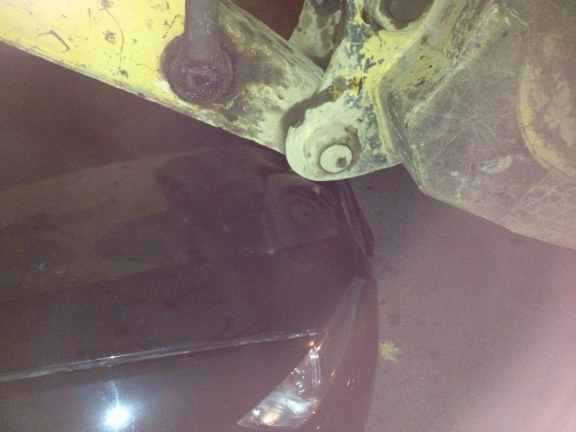 Close up of backhoe resting on (aka smashing) BMW hood.