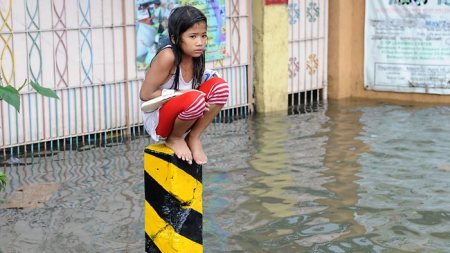 Filipina girl crouches on cement pillar to avoid flood waters Filipina girl crouches on cement pillar to avoid flood waters