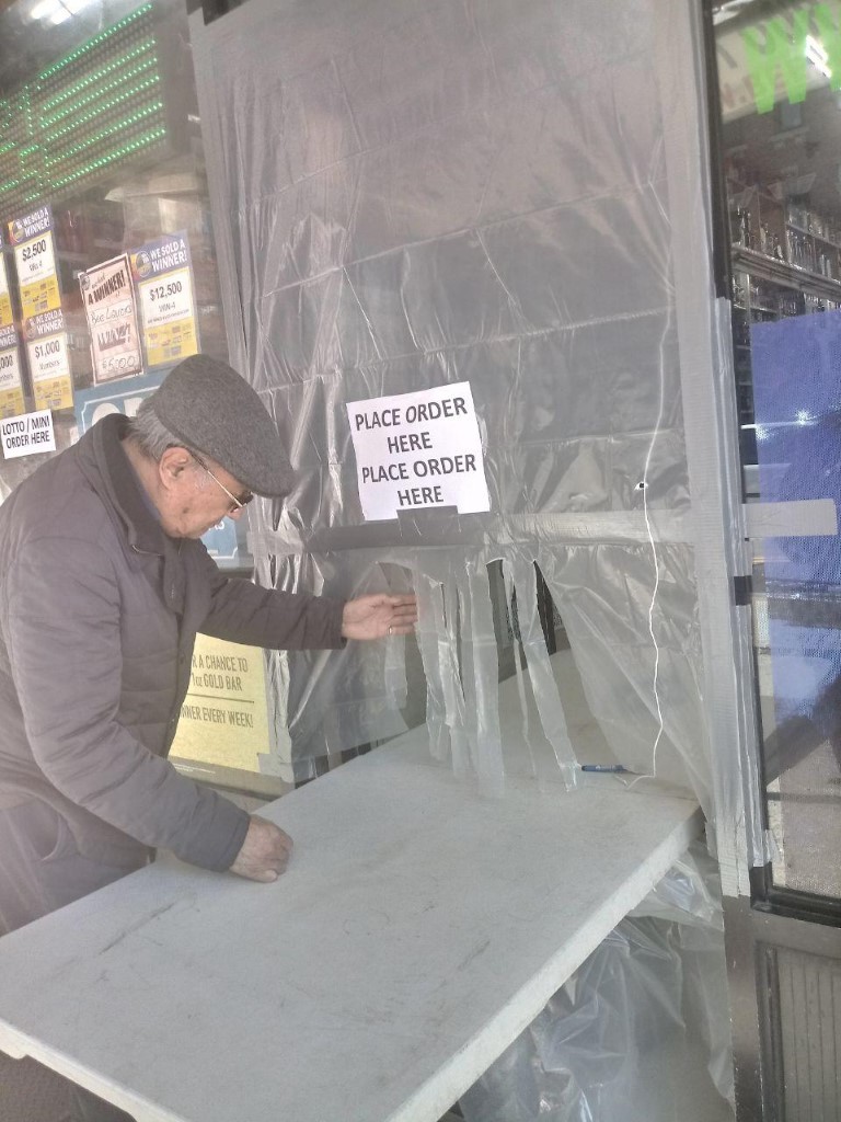 Plastic shielding and a sign at the entrance of a liquor shop requiring customers to remain outside